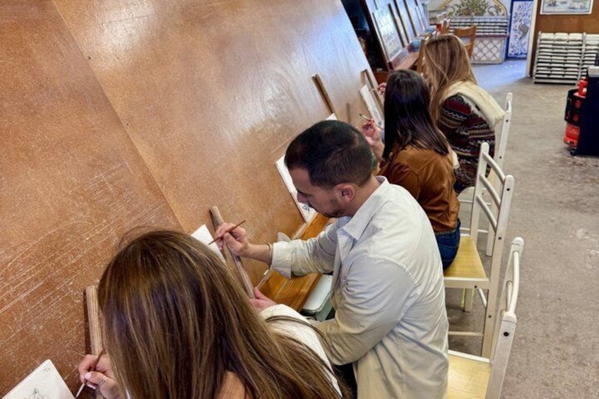 People seated at tables, engaged in drawing or painting activities. 4