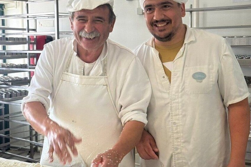 Two people in a bakery, one wearing an apron and the other in a chef's hat, with shelves of baked goods in the background. 3