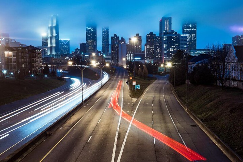 A city skyline at dusk with illuminated buildings and a multi-lane highway with light trails. 2