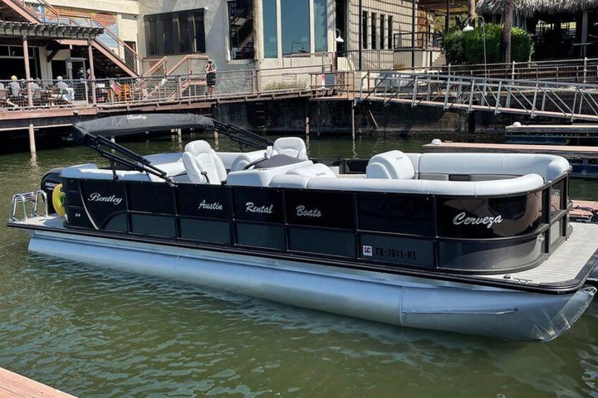 A boat docked at a marina with a covered seating area and a name 'Austin Rental Boats' visible. 3