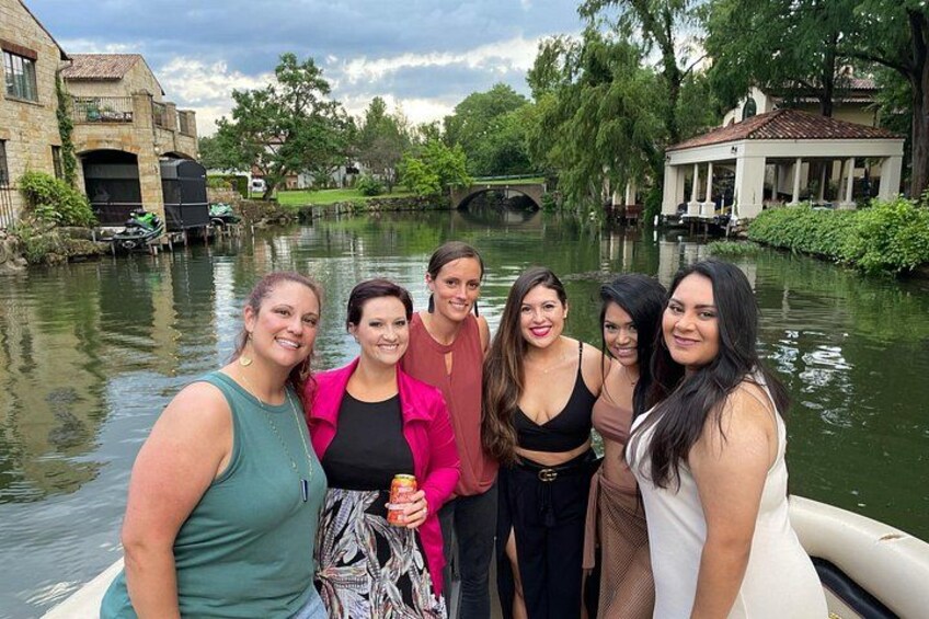 A group of people on a boat near a canal with buildings and greenery in the background. 2
