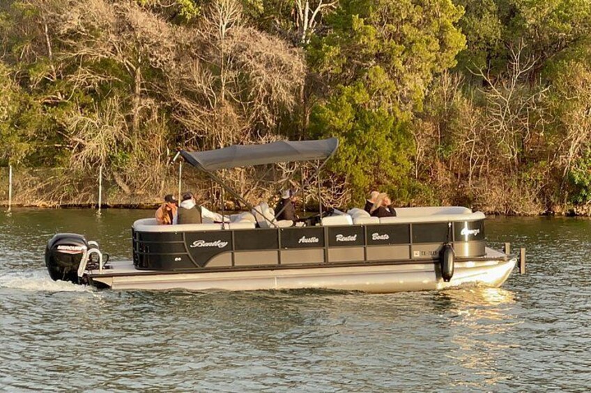 A motorboat with a canopy, passengers, and a wooded shoreline. 2