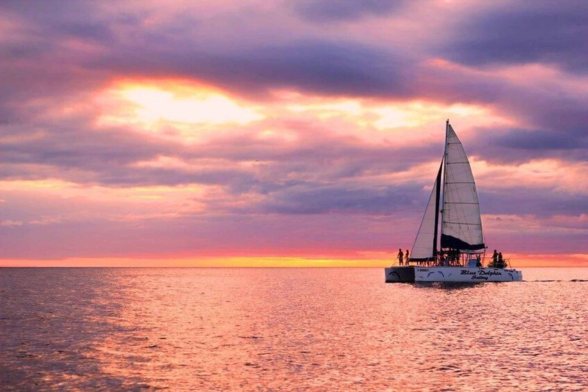 A sailboat named 'Blue Dolphin' sailing on calm waters during sunset. 2