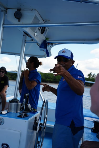 A person in a blue shirt and cap on a boat, pointing towards the water. 5