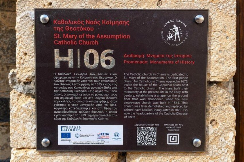 A historical plaque mounted on a stone wall, detailing the St. Mary of the Assumption Catholic Church in Chania, Greece. 2