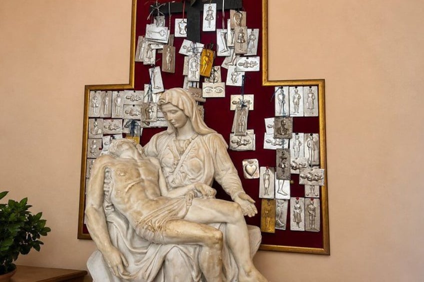A marble sculpture of a woman holding a child, surrounded by framed sketches on a wall. 4
