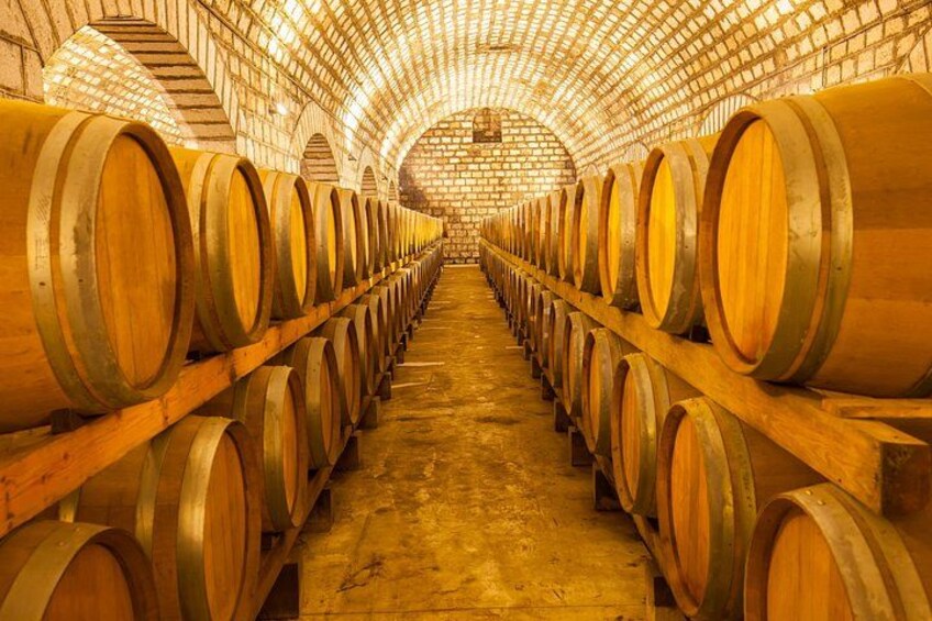 A long row of wooden wine barrels in a brick-walled cellar. 2