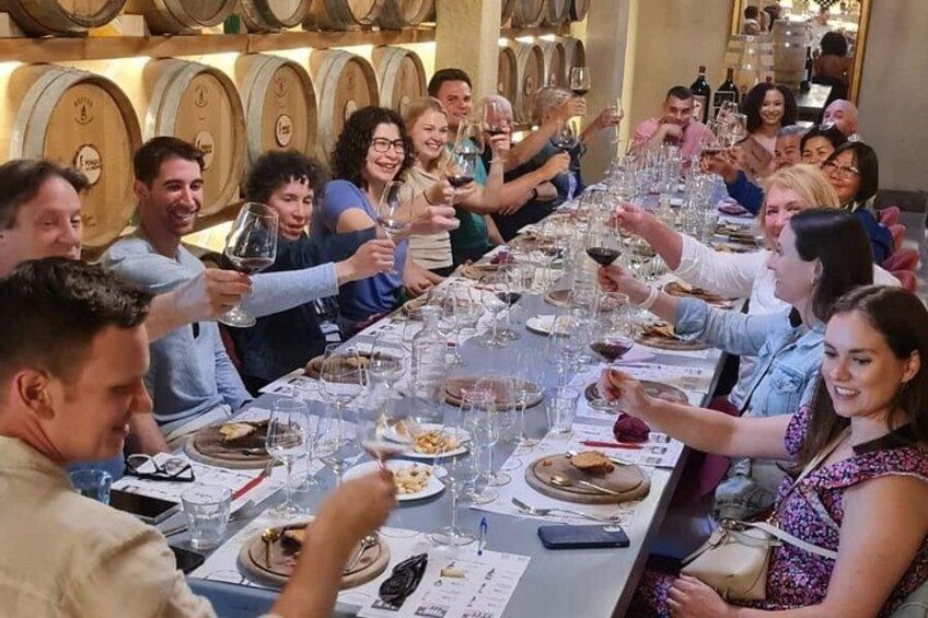 A group of people toasting at a long dining table in a restaurant with wine glasses and plates of food. 2