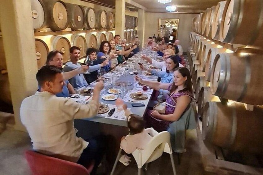 A group of people dining at a long table in a cellar with wine barrels. 3