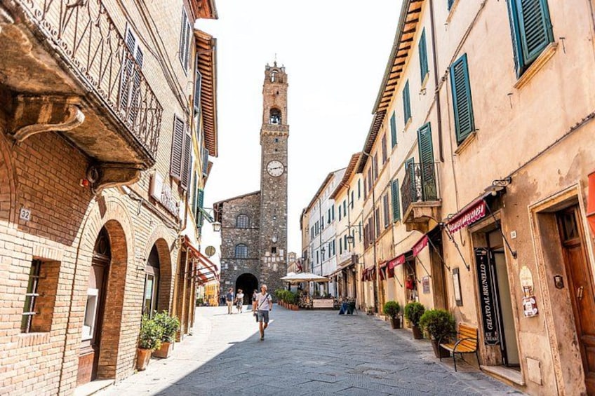 A cobblestone street with historic buildings, a clock tower, and a person walking. 1