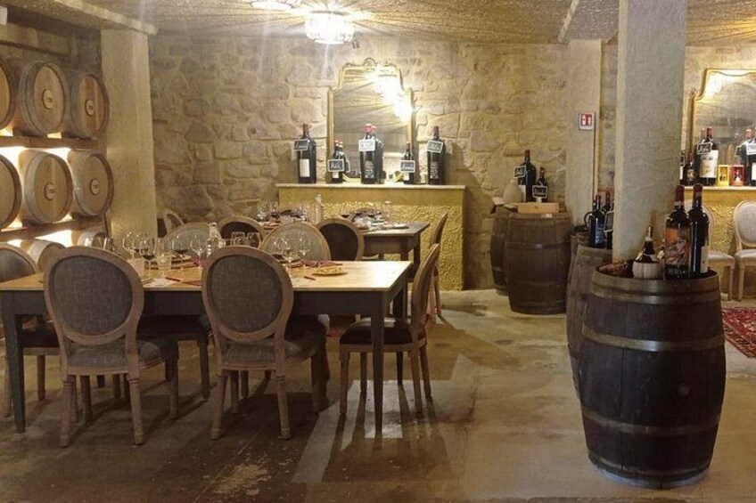 A rustic cellar with stone walls, wooden barrels, and a long dining table. 4
