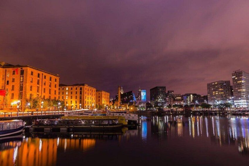 A nighttime cityscape with illuminated buildings, a river reflecting lights, and a bridge with a boat. 2