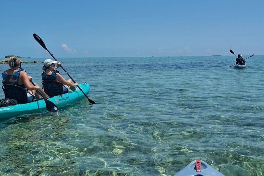 Two people kayaking on clear water, with another kayak in the distance. 1