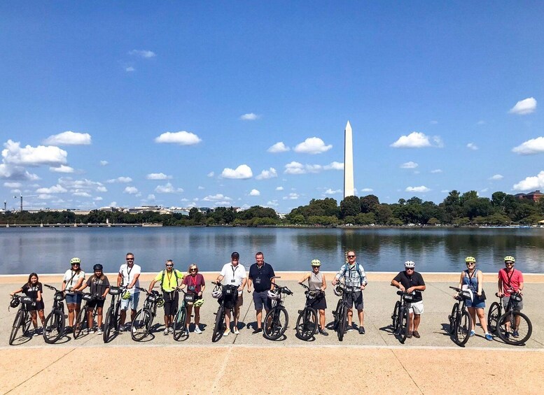 Un grupo de ciclistas junto a un cuerpo de agua, con el Monumento a Washington al fondo. 3
