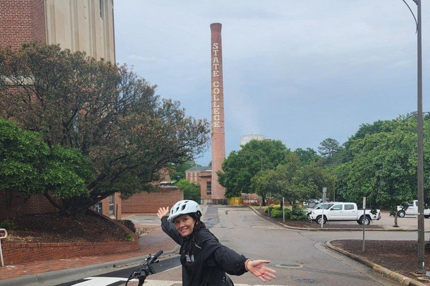A person on a bicycle with a helmet, a brick building, and a tall chimney with the text 'STATE COLLEGE' on it. 4