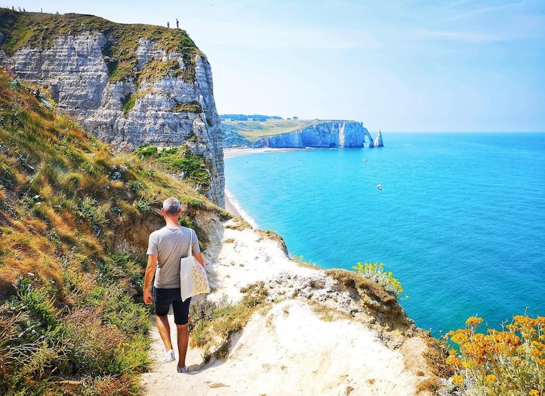 A man walking on a coastal path with cliffs and a beach. 3