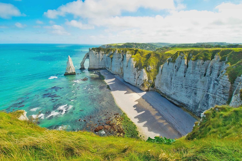A coastal landscape with white cliffs, a sandy beach, and a clear blue sea. 1