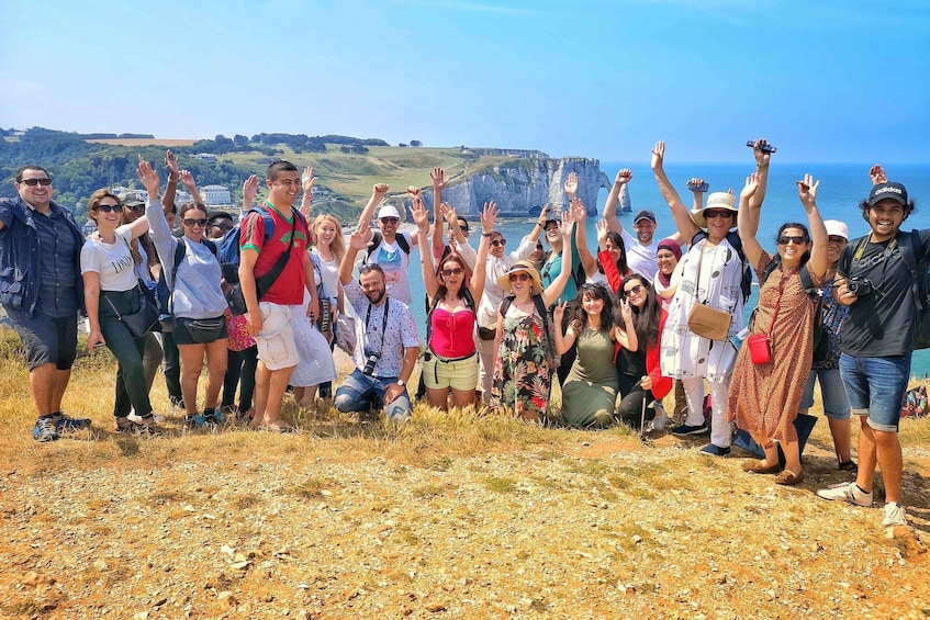 A group of people on a rocky hillside with their hands raised, overlooking a coastal landscape with cliffs and the sea. 5