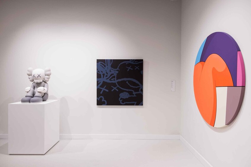 A minimalist art gallery with a white sculpture on a pedestal, a framed abstract painting, and a colorful geometric sculpture on the wall. 2
