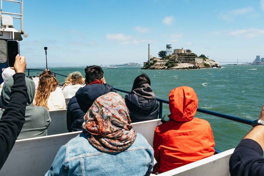 People on a boat, a lighthouse, and a rocky island with buildings. 1