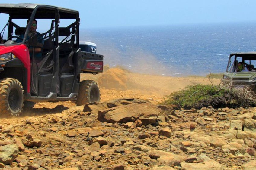 A red off-road vehicle on a rocky terrain with a body of water in the background. 2