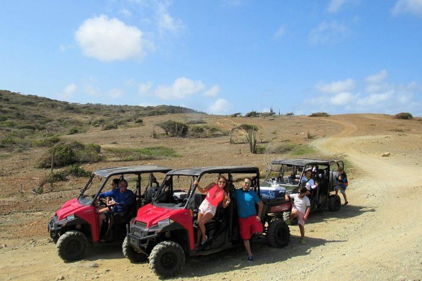 A group of people in off-road vehicles on a dirt road in a hilly, open landscape. 1