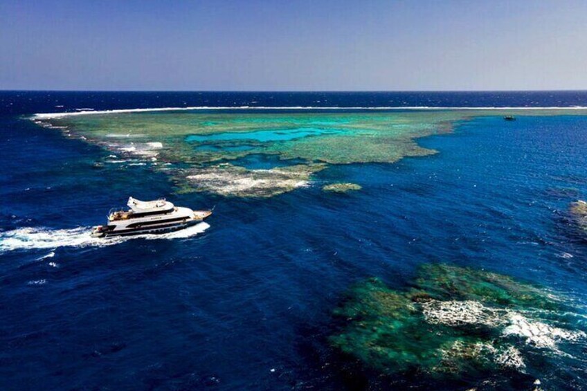 A boat on a clear blue sea with coral reefs and a distant island. 1