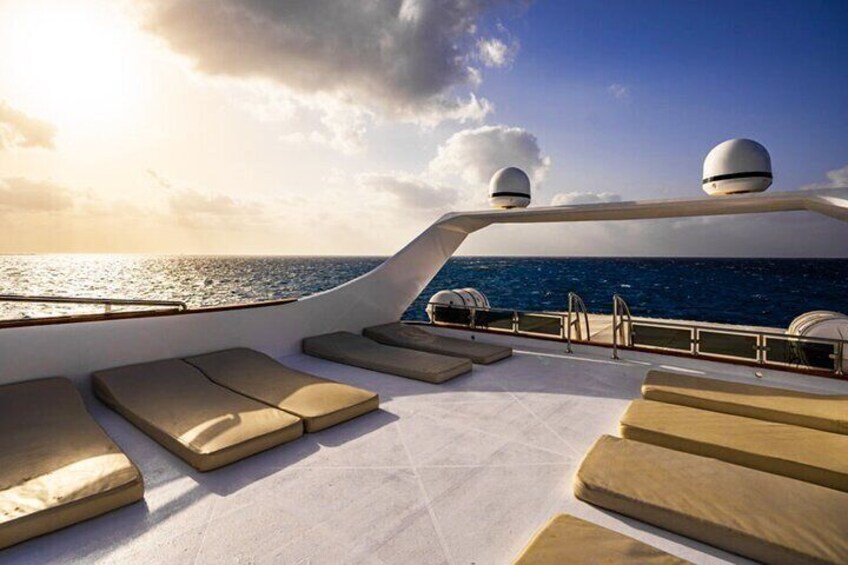 A sunlit deck with lounge chairs and a railing overlooking the ocean. 3