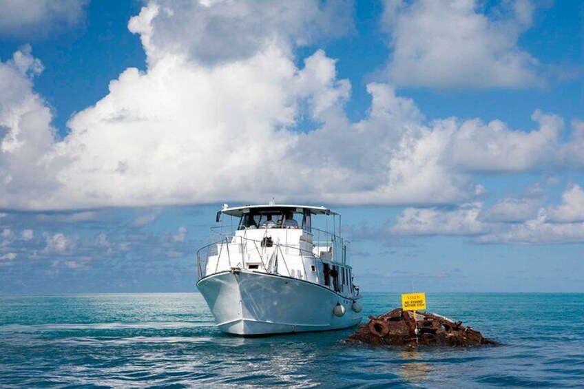 A boat on calm waters with a rocky outcrop and a sign in the foreground. 3