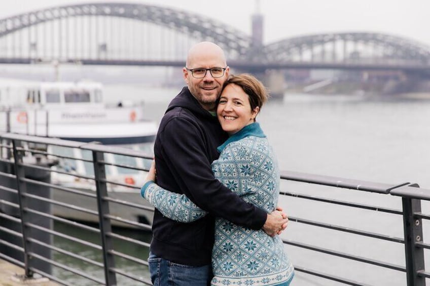 A couple embracing on a bridge with a boat in the background. 3