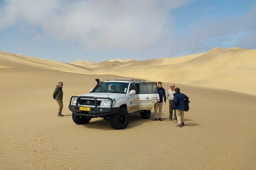 Een witte SUV geparkeerd op een duin in de woestijn, met vier mensen eromheen. 3
