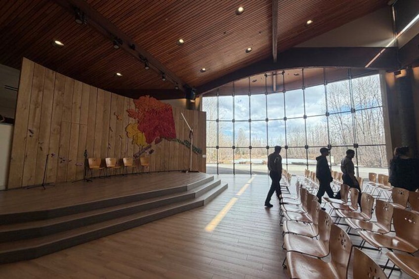 A large hall with wooden paneling, a stage, and rows of chairs. 2