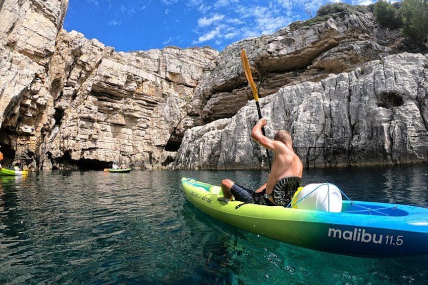 A person kayaking on a clear day with rocky cliffs in the background. 1