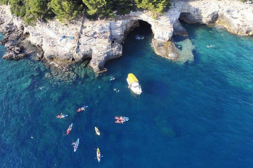 A coastal area with clear blue water, a rocky cliff, and a cave entrance. 2