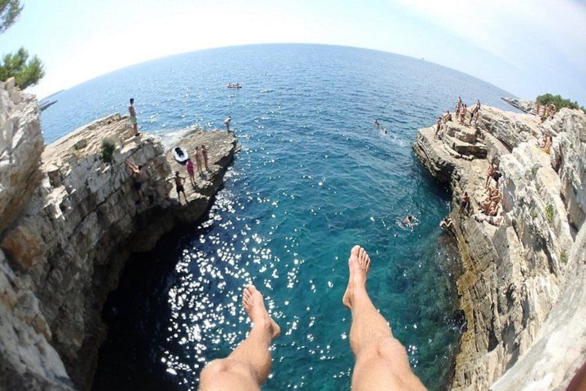 A person's feet dangling over a rocky cliff edge with the sea below. 5