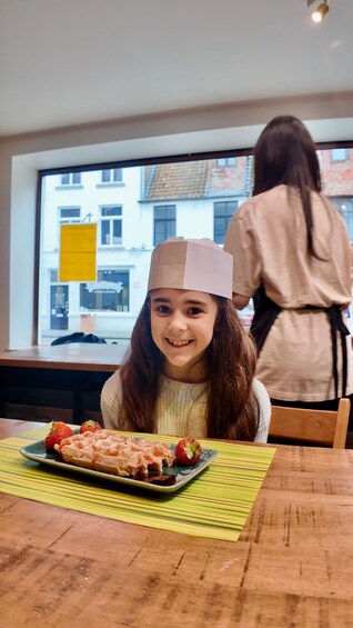 Una persona con un cappello di carta seduta a tavola con un waffle e fragole. 5