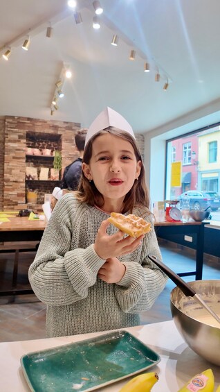 Una persona con gorro de papel, sosteniendo un bocado, con un tazón y un plato verde sobre la mesa. 2