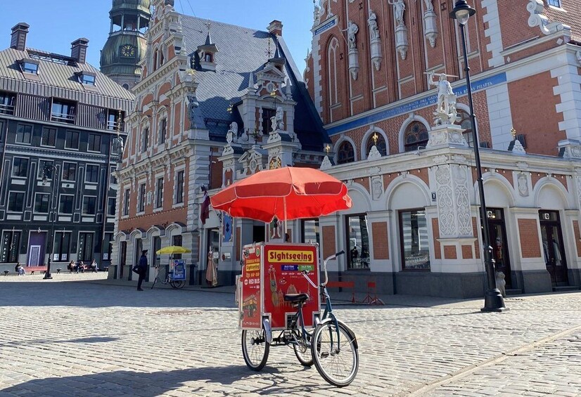 A historic building with ornate architecture and a red umbrella cart labeled "Sightseeing" in front. 2