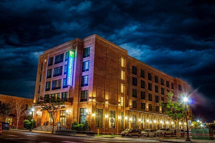 A multi-story hotel with illuminated signage, a brick facade, and a parking lot at night. 1
