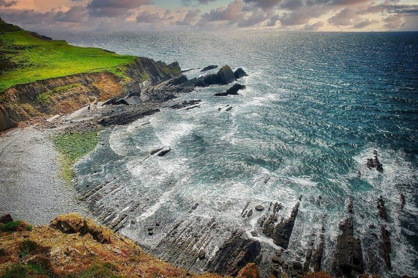 A coastal landscape with rocky cliffs, a grassy area, and the ocean. 1