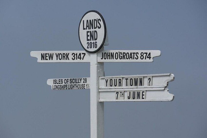 A directional signpost with multiple signs, including 'LAND'S END 2016,' 'NEW YORK 3147,' 'JOHN O'GROATS 874,' 'ISLES OF SCILLY 28,' 'LONGSHIPS LIGHTHOUSE 1 1/2,' and 'YOUR TOWN? 7TH JUNE.' 4
