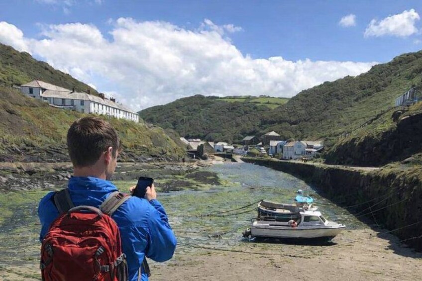 A person taking a photo of a boat on a riverbank with houses in the background. 1