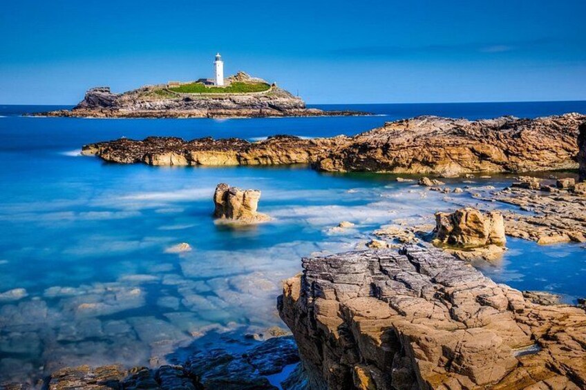A coastal landscape with a lighthouse on a rocky outcrop, clear blue water, and distinctive rock formations. 5