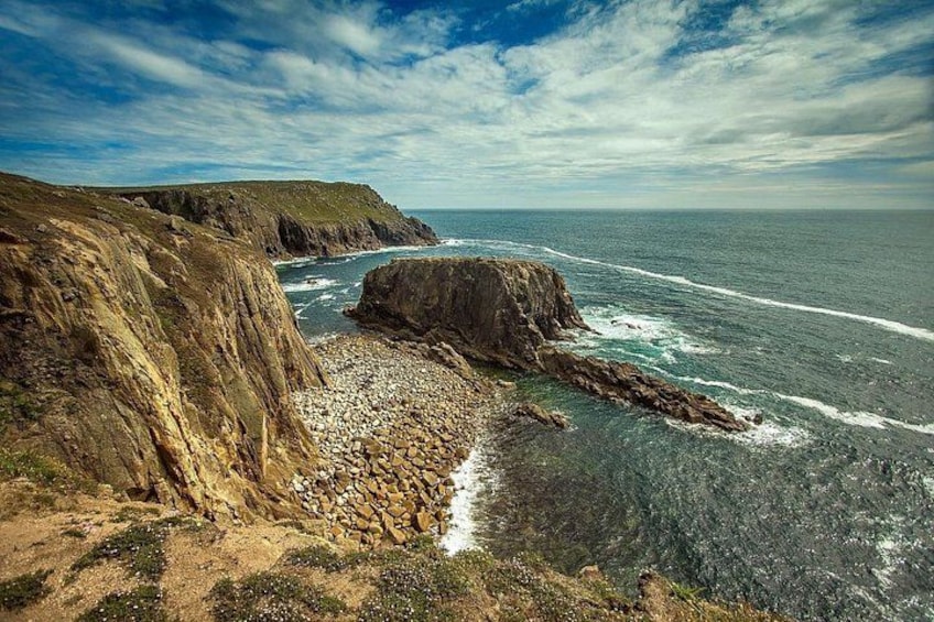 A coastal landscape with rocky cliffs, a pebble beach, and the ocean. 3