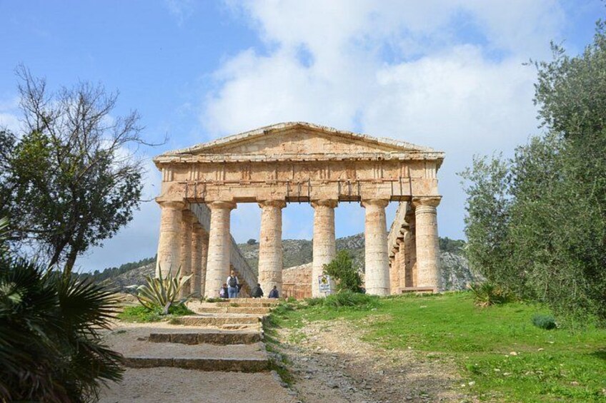 An ancient Greek temple with columns, surrounded by greenery and a clear sky. 1