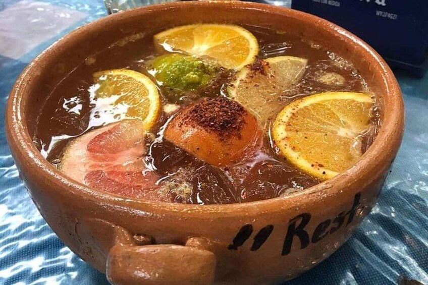 A clay pot with a stew containing meat, lemon slices, and herbs. 2