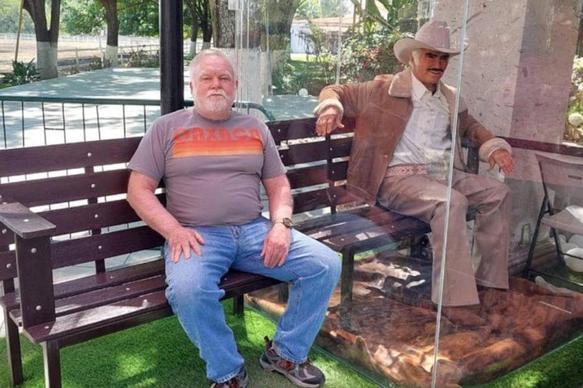 A man sitting on a bench with a statue of a cowboy in the background. 5