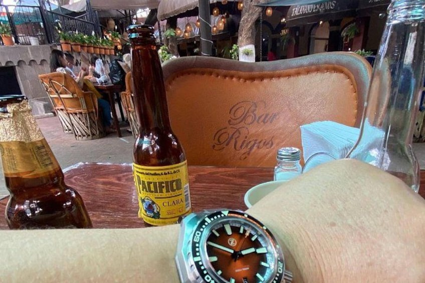 A table with a bottle of Pacifico beer, a watch, and a glass of water. 3