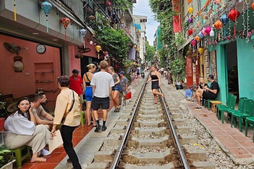 A narrow street with a railway track running through it, people walking and sitting on benches. 3