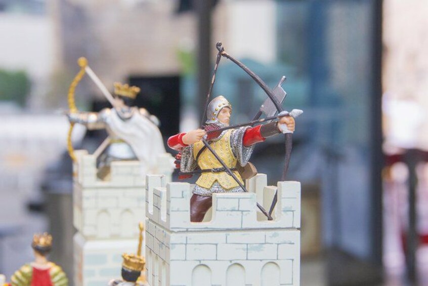 En liten figur som föreställer en riddare på en av tornen på ett slott, ytterligare en figur i bakgrunden och en tredje figur vid tornets fot. 2